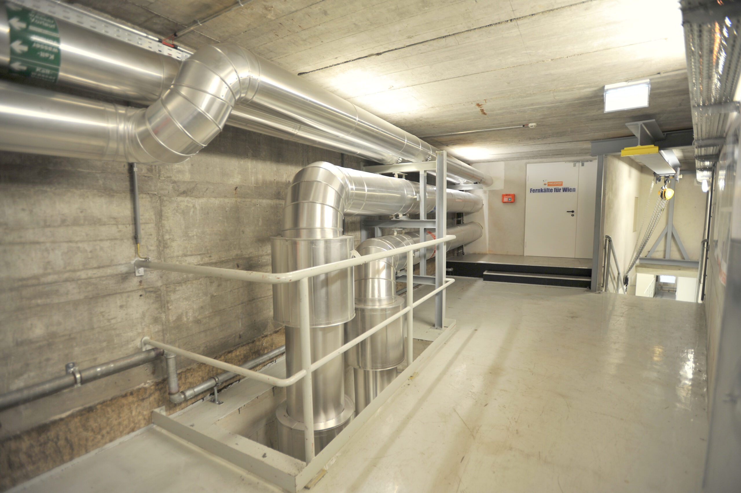 Industrieller Raum mit Metallrohren, Betonwänden und Leuchtstoffröhren. Im Raum steht die Fernkältezentrale Spittelau.